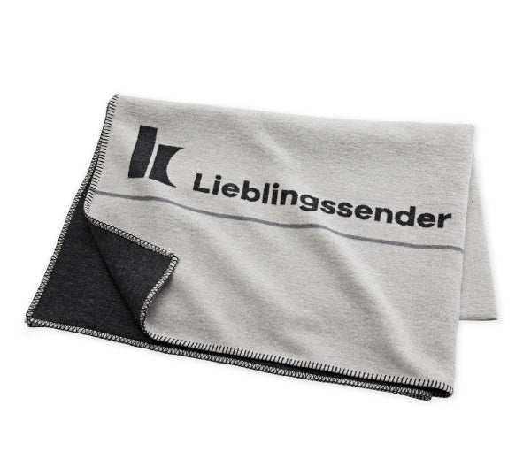 Klassik Radio Kuscheldecke, zusammengefaltet, mit K von Klassik Radio Logo und dem Wort Lieblingssender