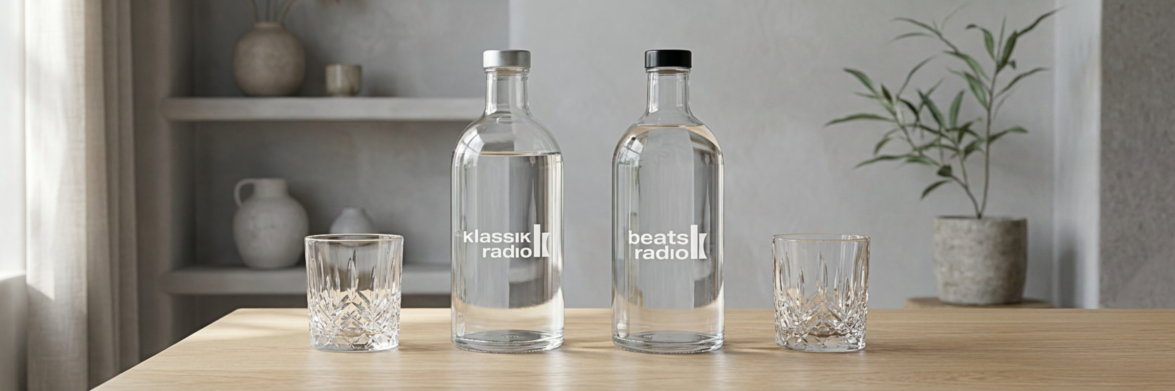 Glasflasche von Beats Radio und Klassik Radio auf einem Holztisch, daneben zwei Gläser