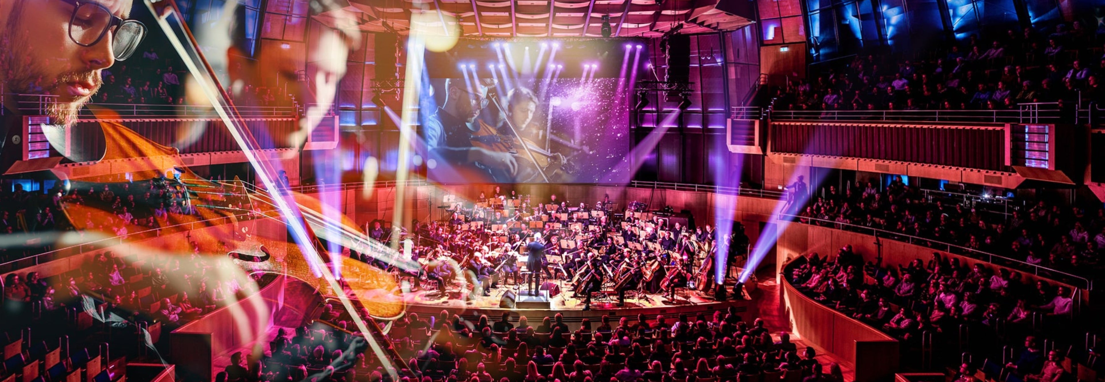 Voller Konzertsaal mit einem großen Orchester auf der Bühne und auf der Leinwand 2 Geiger