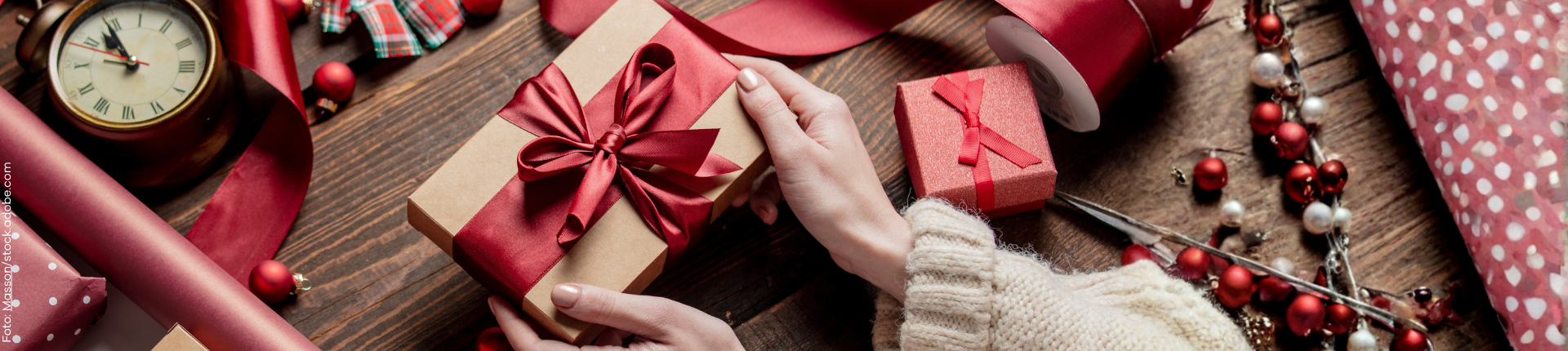 Frauenhände halten Geschenk mit roter Schleife in der Hand