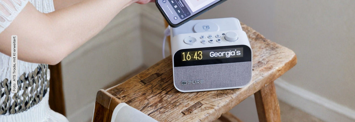 Pure Moment Charge Radiowecker mit Ladestation auf einem Holzbänkchen. EIne Frau legt gerade ihr Handy auf die Ladestation