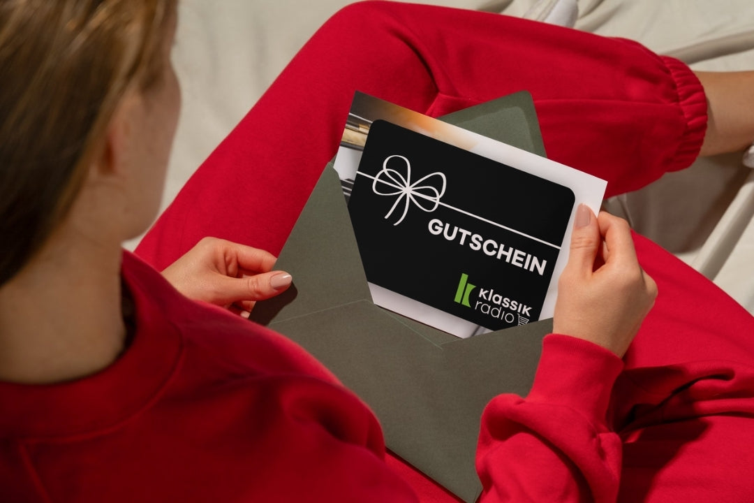 Frau im roten Jumpsuit öffnet Briefumschlag mit Klassik Radio Shop Gutschein