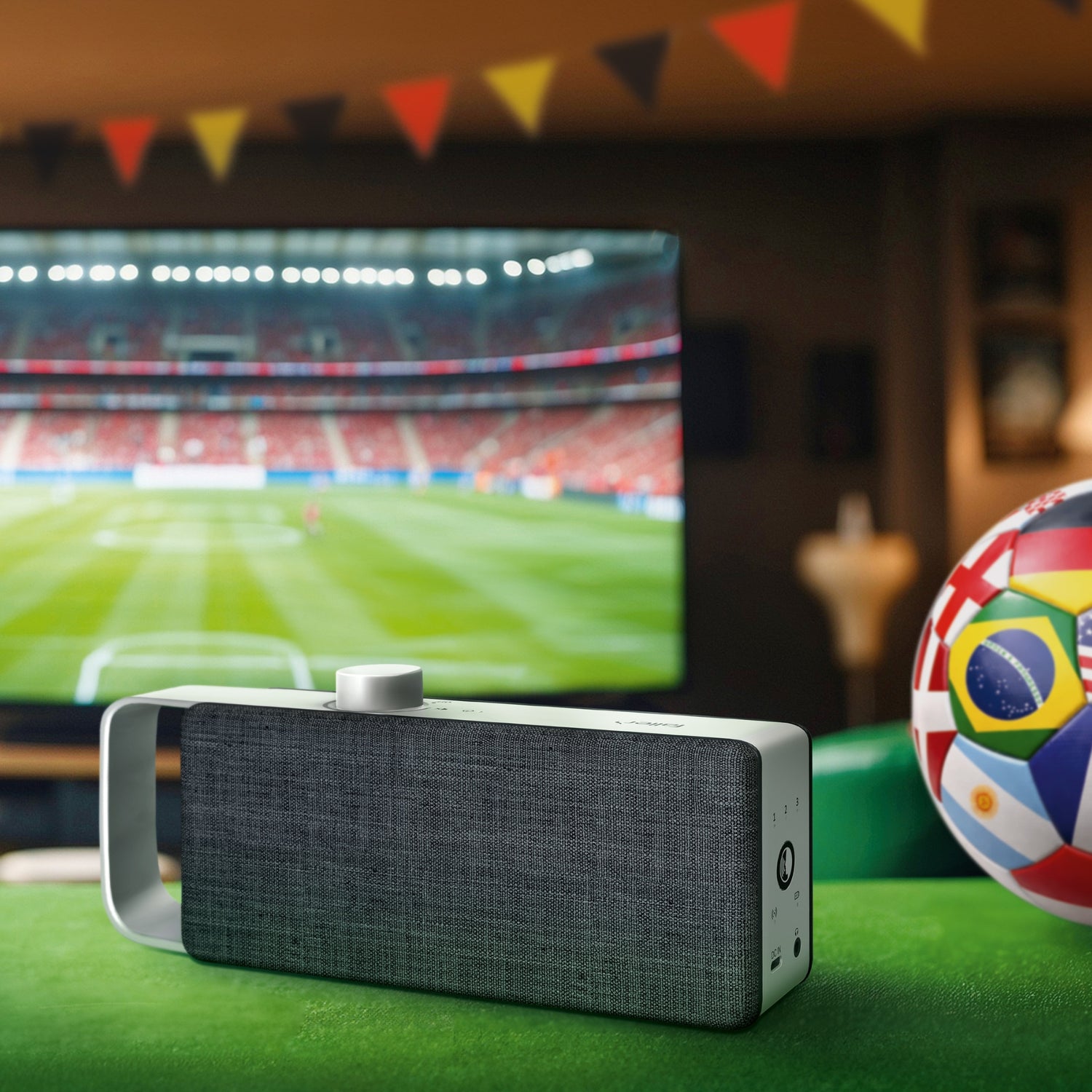 TV Sprachverstärker in Fuball WM Optik, im Hintergrund ein TV-Bildschirm, der ein Fußballstadium zeigt